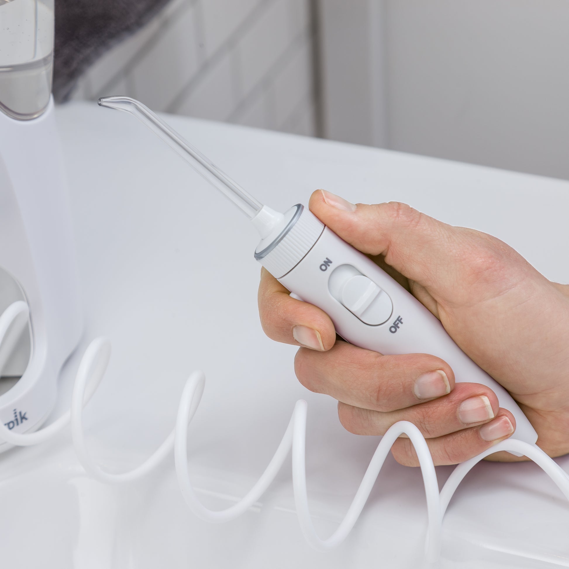 Hand holding the handle and attached tip of the white Ultra Plus countertop water flosser, extended by its coiled hose.