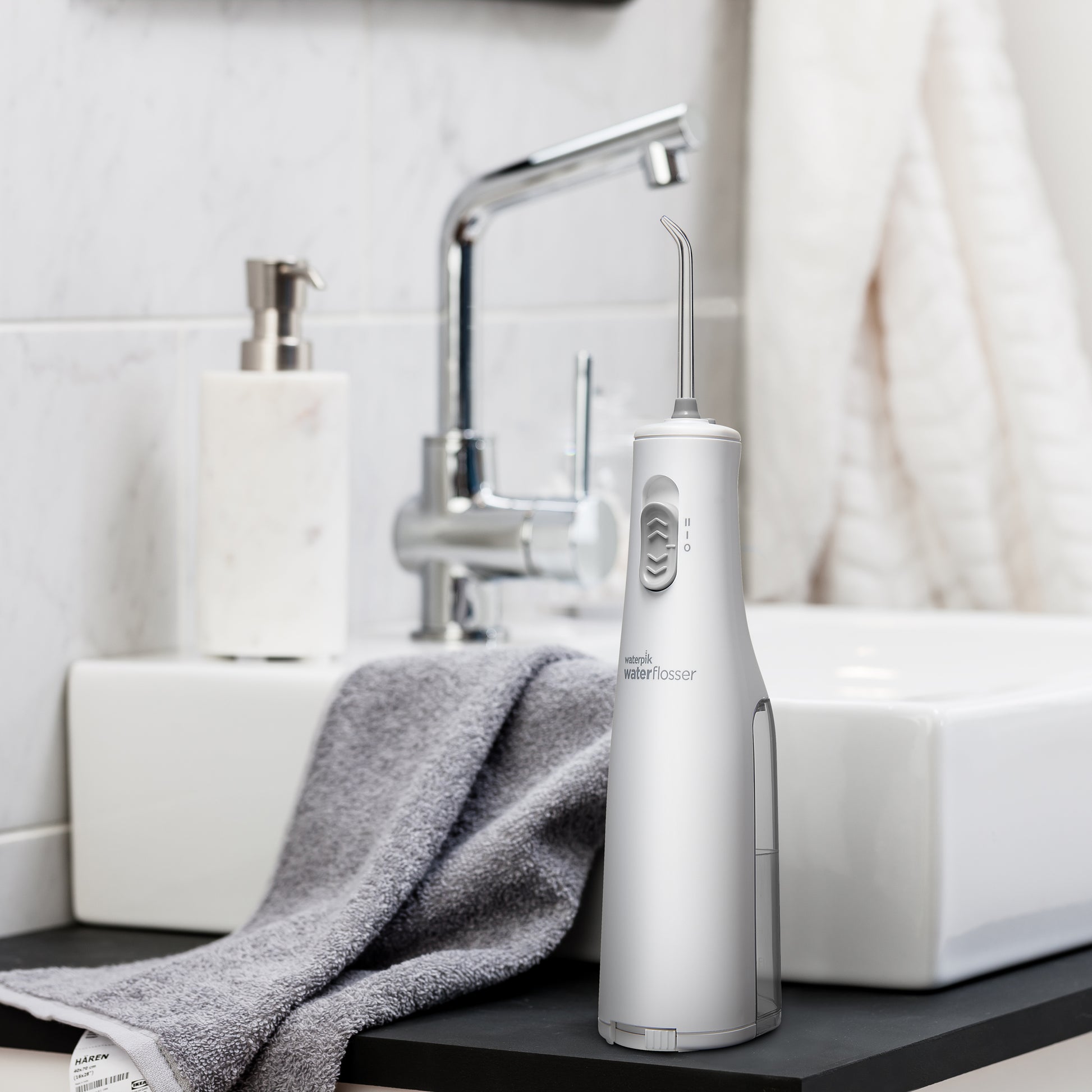 White Cordless Express handheld water flosser on a bathroom sink.